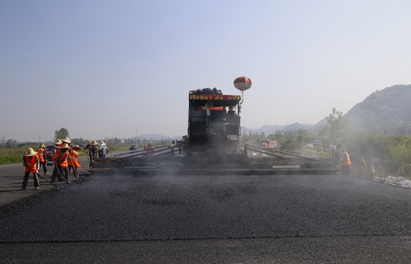 2019年8月，宜春經(jīng)開區(qū)S311路面攤鋪現(xiàn)場(chǎng)，工友們輔助路面兩側(cè)的分料、補(bǔ)窩等作業(yè)